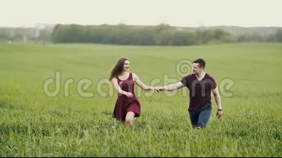 在燕麦地里的一对可爱的夫妇美女边走边高兴地跳黑发女人头发摇曳慢动作视频的预览图