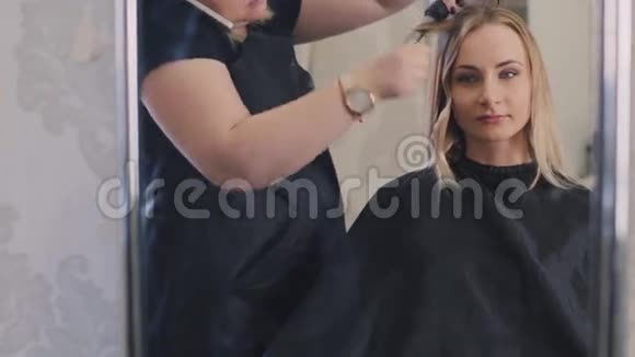 专业美发师在美容院做发型用直发器理金发美女长发视频的预览图
