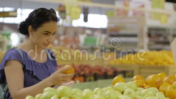 漂亮的年轻女人深色头发的女人在超市里选择水果新鲜的橙色购物和人的概念股票视频的预览图