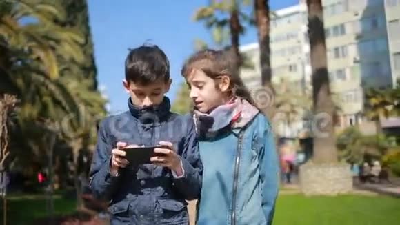 孩子们沿着公园的林荫道散步忙着打电话视频的预览图