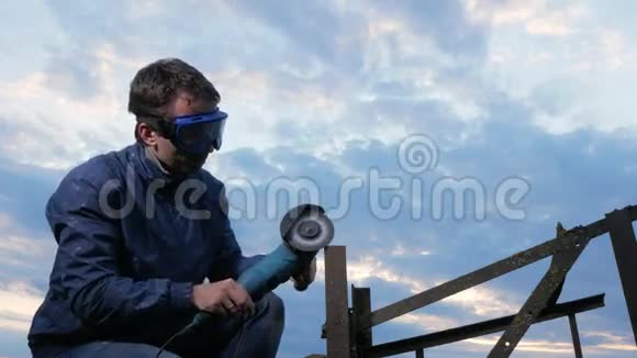 一个年轻人在日落时打磨一台金属角磨机工人后面美丽的天空视频的预览图