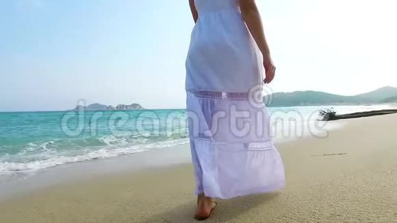 阳光明媚的一天穿着白色连衣裙的女孩在沙滩上散步慢动作视频的预览图