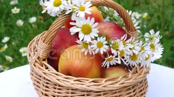 特写镜头漂亮的红苹果放在篮子里在一片开花的雏菊田野里草坪上在篮子上一个花环视频的预览图