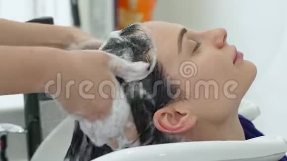 理发店客户用专业洗发水洗头理发师用手按摩头部视频的预览图