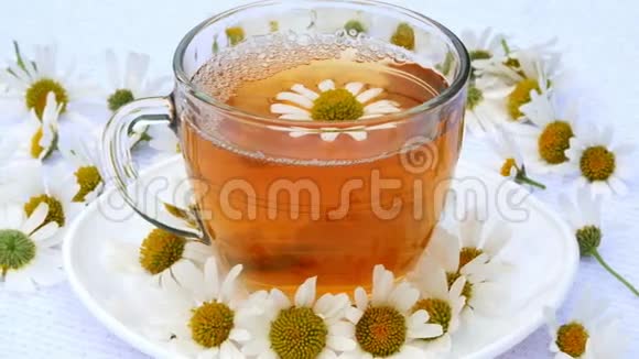 特写透明玻璃杯上有洋甘菊茶放在白色茶托上一切都用洋甘菊花装饰视频的预览图
