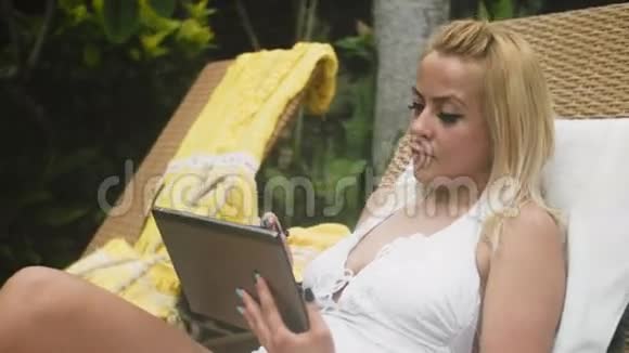 穿着泳衣的金发女郎躺在躺椅上拿着平板电脑视频的预览图