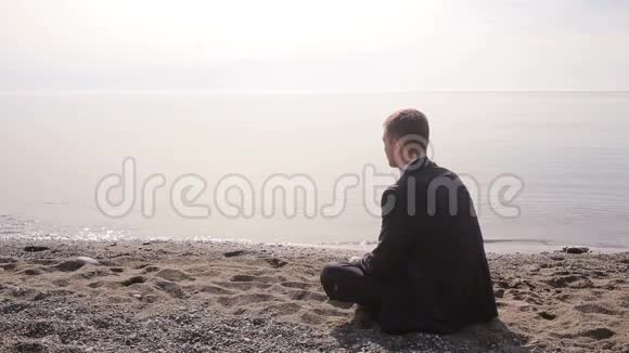 穿西装的商人坐在沙滩上把石头扔进水里视频的预览图