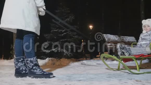 在傍晚的冬季公园里母亲把一个小女儿卷在雪橇上视频的预览图