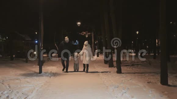 可爱的年轻一家人在冬夜公园散步视频的预览图