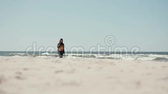 一位年轻的黑发孕妇正在一个刮风的日子里沿着海岸和平地散步视频的预览图