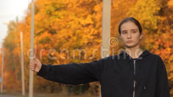 一个穿着兜帽的女孩在高速公路上搭便车对抗黄绿橙色的森林视频的预览图