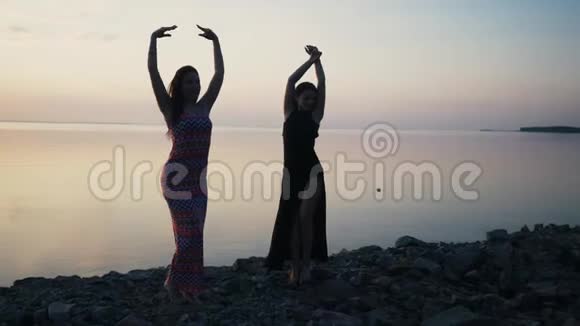在日落时分穿着黑色长裙在沙滩上跳舞的无忧无虑的女人视频的预览图
