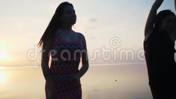 在日落时分穿着黑色长裙在沙滩上跳舞的无忧无虑的女人视频的预览图