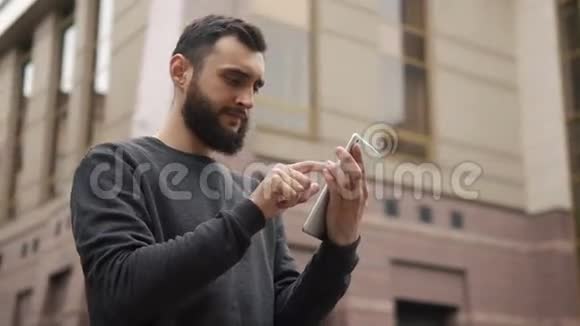快乐的胡子年轻人日落时在街上使用平板电脑视频的预览图