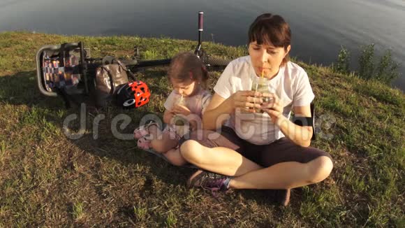 妈妈和女儿坐在池塘的岸边喝一杯绿色的鸡尾酒视频的预览图