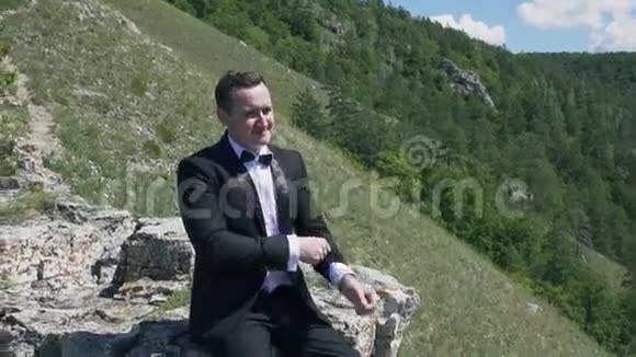 新郎坐在背景山景的岩石上视频的预览图