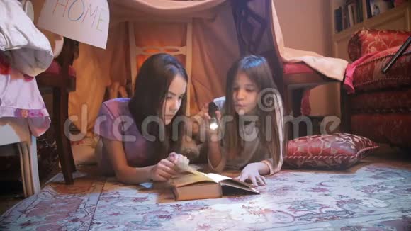 两个可爱的姐妹躺在地板上用手电筒看书视频的预览图