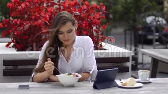 布鲁内特女士吃沙拉看着她的平板电脑上的东西而她坐在餐厅前红花视频的预览图