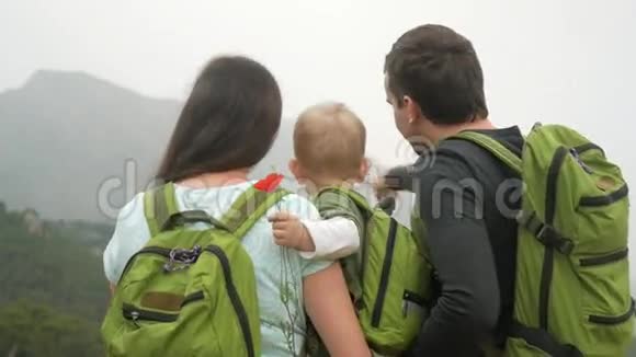 一个年轻的旅人家庭带着一个回头看群山每个人都有相同的绿色背包视频的预览图