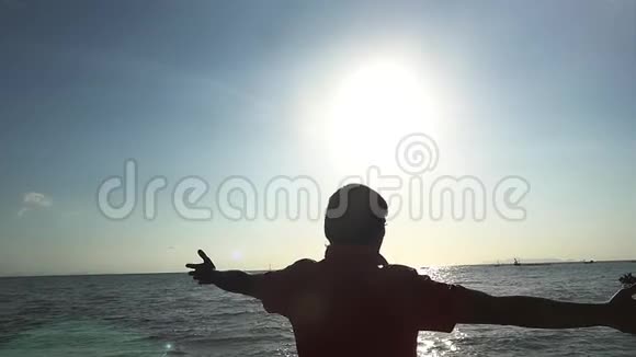 快乐的年轻人在海边的海滩上缓慢地举手太阳闪耀着美丽的透镜耀斑视频的预览图