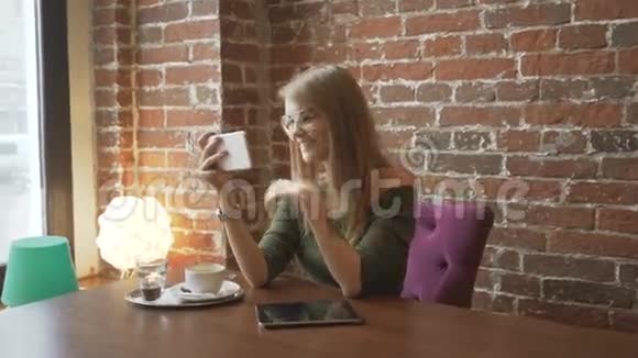 年轻的微笑女人在咖啡店里用智能手机进行视频对话视频的预览图