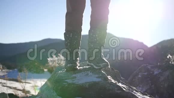 穿着冬靴站在白雪覆盖的岩石上背景是阳光下美丽的山脉带有镜头效果视频的预览图