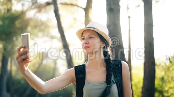 有趣的戴帽子的旅游女孩在旅行和搭便车期间用智能手机相机自拍照片视频的预览图