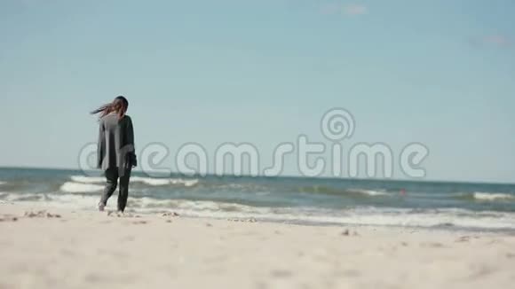 一位年轻的黑发孕妇在凉爽的一天赤脚在沙滩上行走视频的预览图
