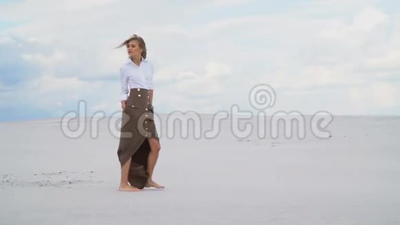 一个穿裙子和衬衫的女孩沿着沙漠缓慢地走着视频的预览图