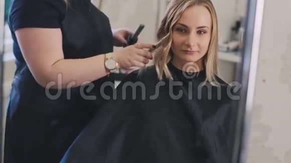 专业美发师在美容院做发型用直发器理金发美女长发视频的预览图
