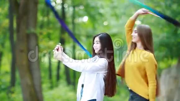 女体操运动员在公园里用蓝色丝带练习女朋友拿着手机视频的预览图