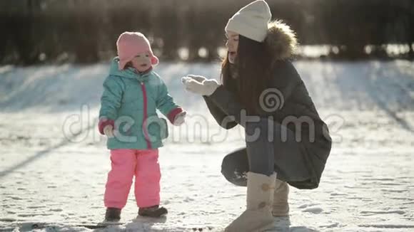 年轻的母亲在手里吹雪小女儿在看雪花女孩子在玩视频的预览图