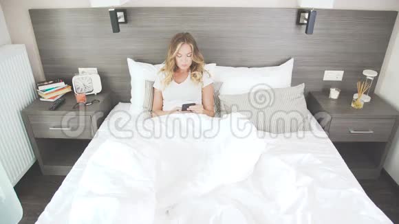 漂亮的女人在床上上网使用小玩意智能手机视频的预览图