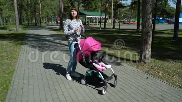 年轻的母亲带着婴儿车在公园散步视频的预览图