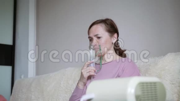 一个女人坐在家里的沙发上通过吸入器吸入面部吸入面罩在家治疗视频的预览图