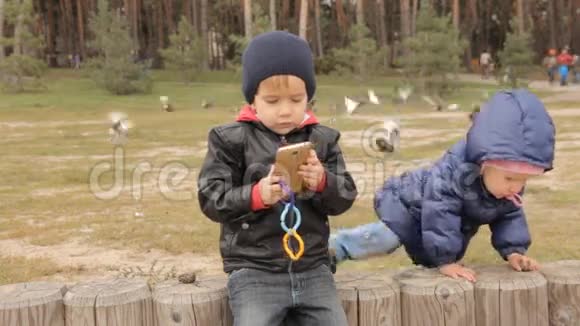 一个女孩爬在篱笆上一个男孩坐在那里他在智能手机上按下按钮视频的预览图