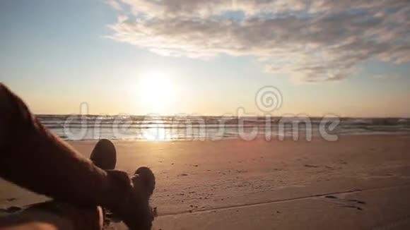 一个人在沙滩上躺着享受美丽的柔和日落时交叉双腿的景色视频的预览图
