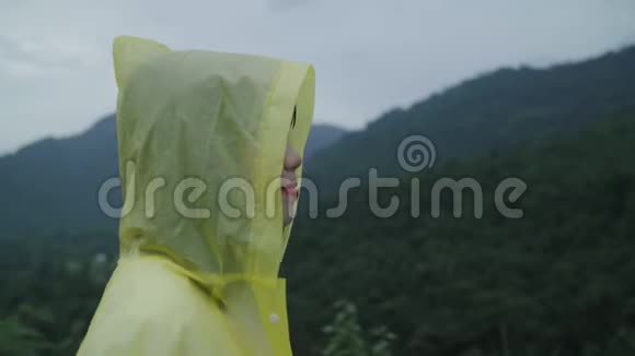 年轻的亚洲女人穿着雨衣在森林附近散步一边玩雨感觉很快乐视频的预览图