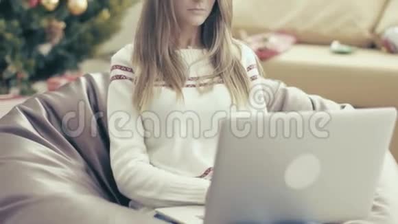 戴圣诞帽的女孩在软椅上用笔记本电脑视频的预览图