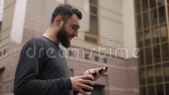 快乐的胡子年轻人在智能手机上聊天在日落时在街上喝咖啡视频的预览图