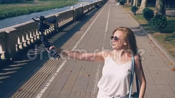 美丽快乐的女博主带着相机领着她的报告文学漫步在度假城市的堤岸上这个视频的预览图