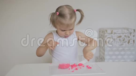 一个小女孩坐在一个明亮的房间的桌子旁雕刻一个粉红色的塑料雕像视频的预览图