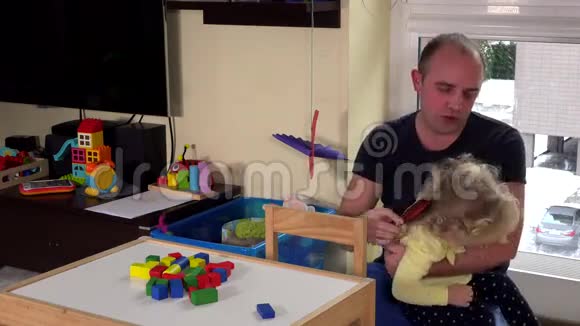 可爱的父亲在家里用刷子梳女儿的头发视频的预览图