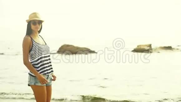 美丽的游客穿着短裤黑白T恤和帽子住在海边在相机上摆姿势视频的预览图
