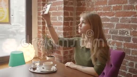美丽的年轻女子正在用智能手机自拍在咖啡馆休息时微笑着视频的预览图