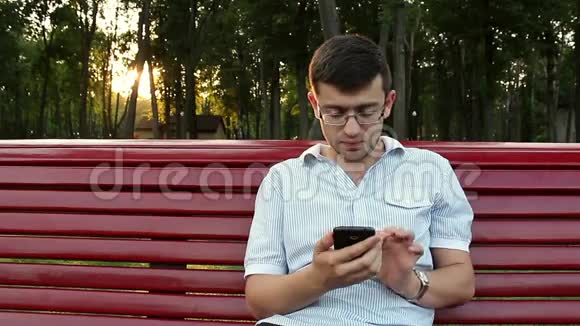 年轻人坐在公园里在你的智能手机上工作视频的预览图