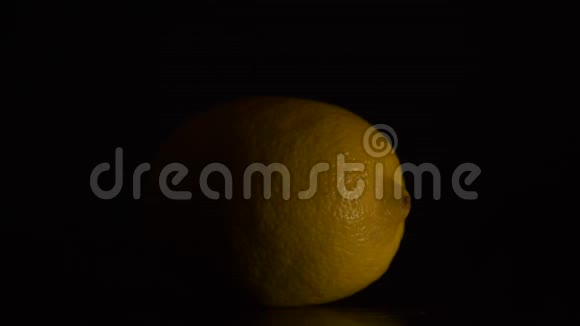 木制桌子上的新鲜柠檬一个新鲜的黄柠檬放在木纹桌子上背景黑色视频的预览图