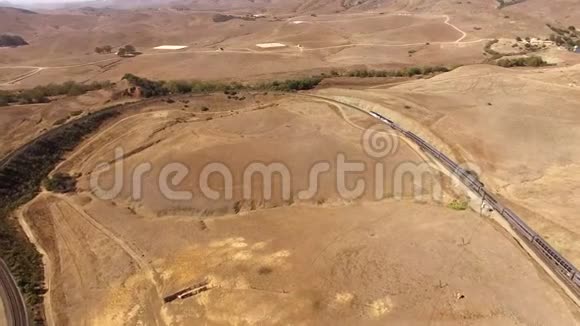 4k空中无人机拍摄的大型现代城市客运列车穿越干沙草原峡谷山沙漠景观视频的预览图