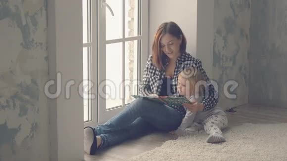 母亲带着小女儿坐在窗户附近读了一本书视频的预览图