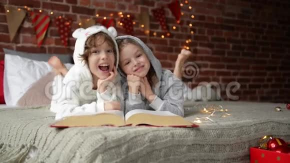 可爱的微笑的姐姐和哥哥在圣诞节的时候看书在家里笑他们在等一个视频的预览图